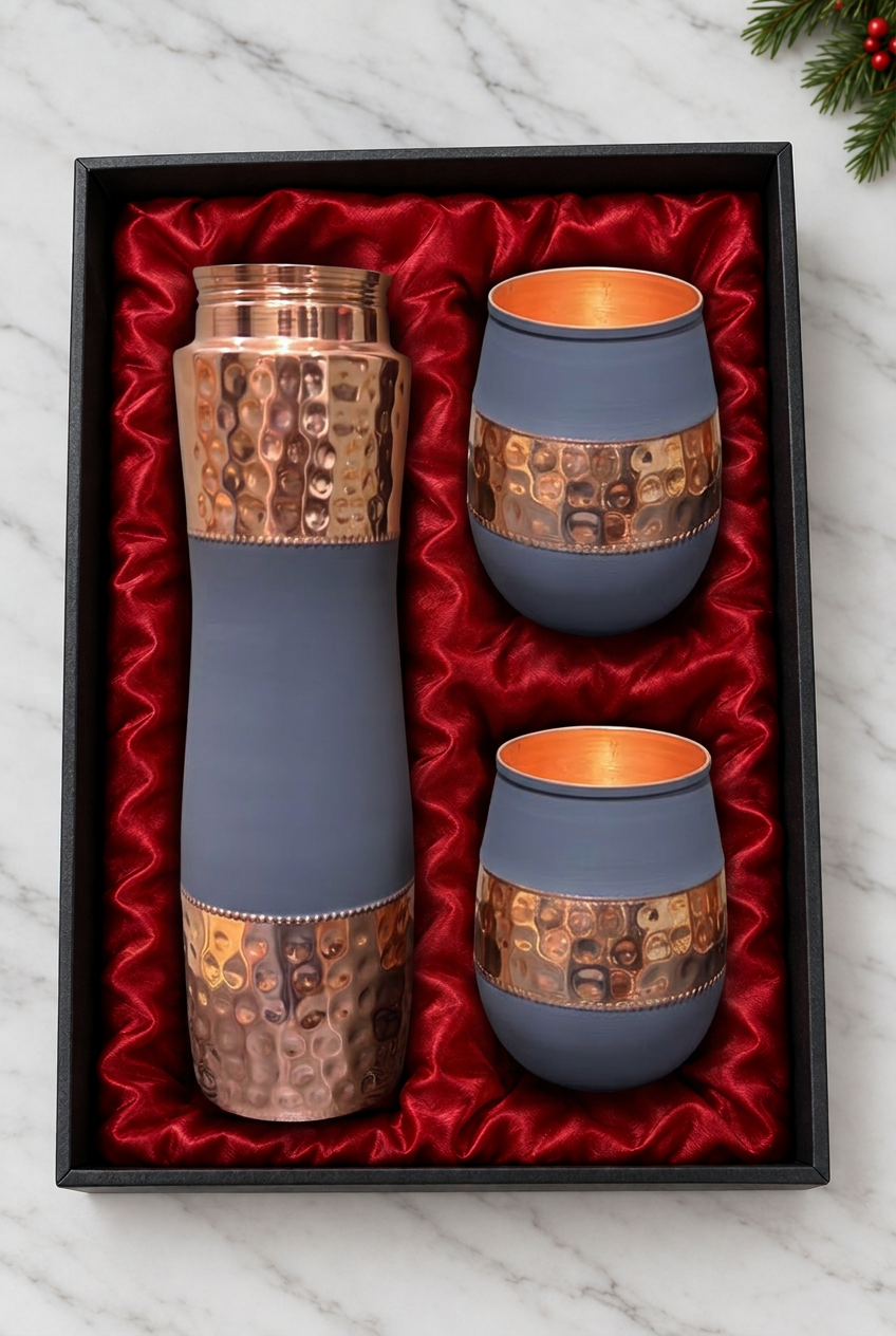 Slate-blue and hammered copper bottle with two rounded tumblers in a red-satin-lined black gift box on white marble